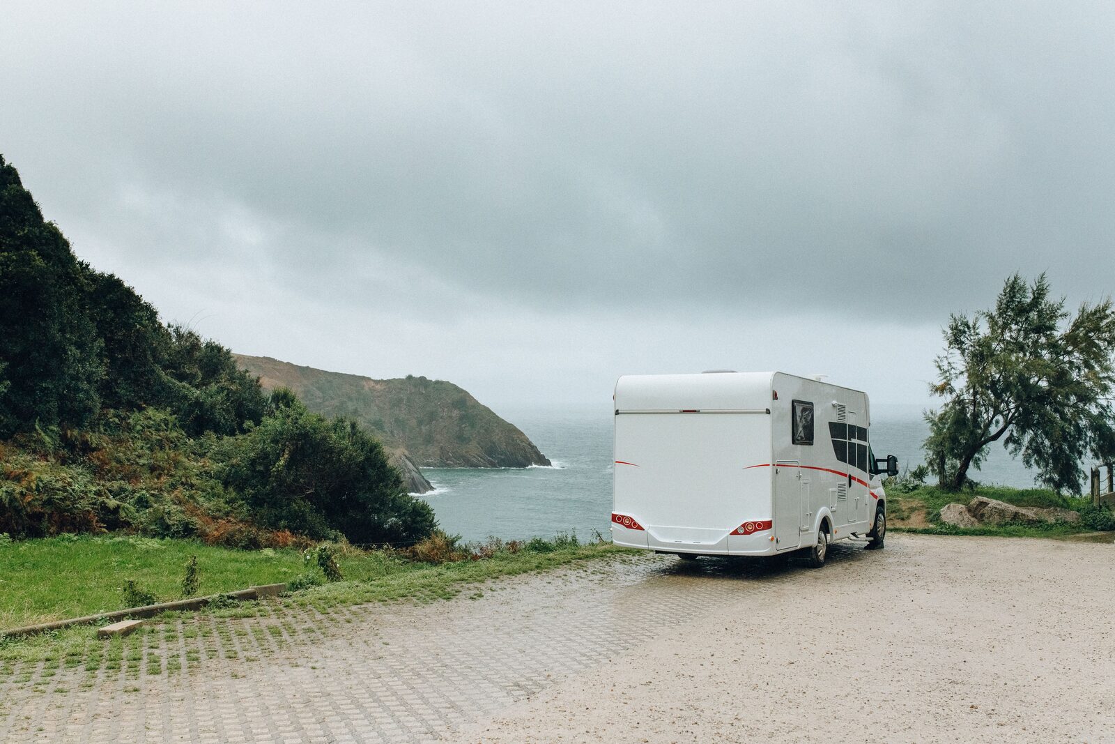 Aire camping-car bord de mer avec caravane stationnée près du rivage sous un ciel nuageux